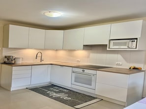 A modern kitchen with white cabinets, a built-in microwave, a coffee maker, and a stainless steel sink.