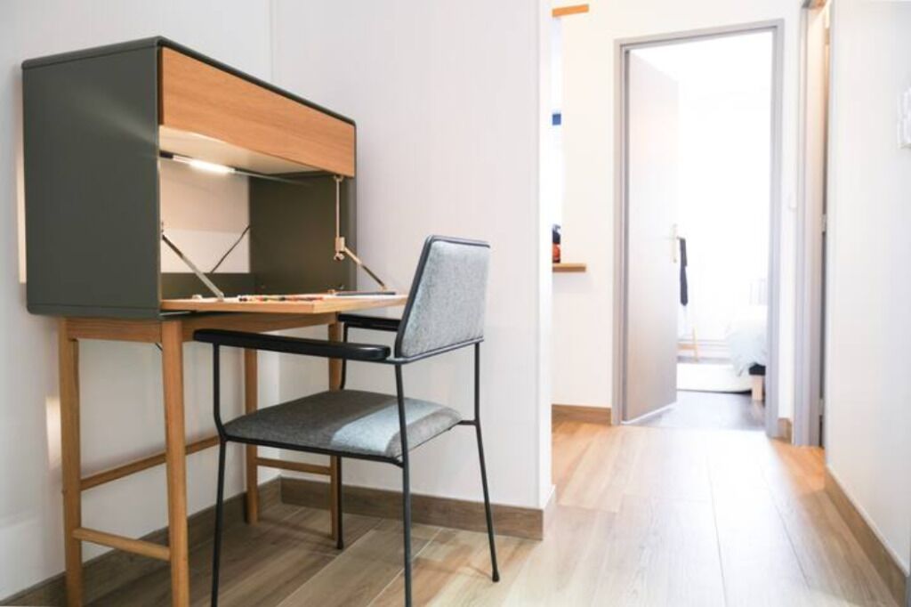 A compact workspace with a desk, chair, and overhead storage unit.