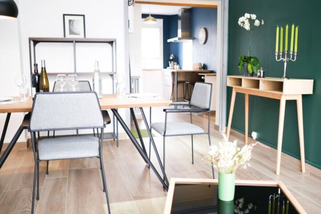 Un comedor moderno con una mesa de madera, sillas tapizadas grises y una mesita auxiliar con un jarrón de flores.