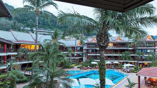 Um resort com vários edifícios, piscina central e vegetação exuberante.