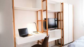 A compact, modern room with a white desk, a laptop, a TV, and a bed.