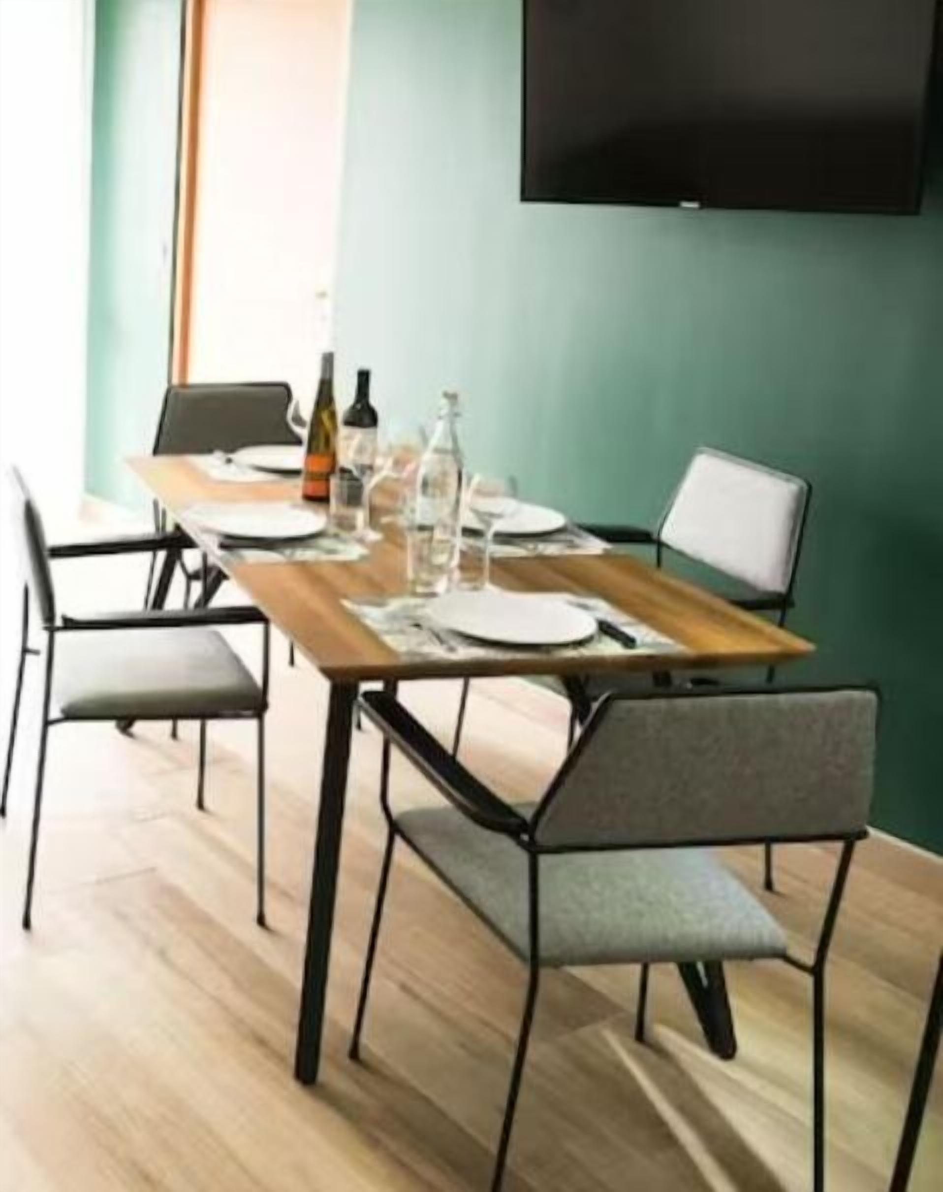 A dining area with a wooden table, metal chairs, and a flat-screen TV mounted on the wall.
