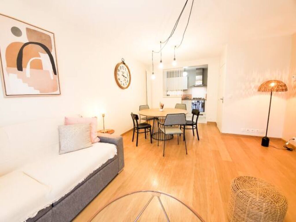 Una sala moderna con sofá, mesa de comedor y sillas. Se observa una zona de cocina al fondo.