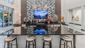 A modern kitchen with a large island, a flat-screen TV, and bar stools. - Relax at Cityline I Premium 2BR in Dallas (Richardson)