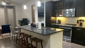 A modern kitchen with dark cabinets, a central island with stools, stainless steel appliances, and pendant lighting. - Relax at Cityline I Premium 2BR in Dallas (Richardson)