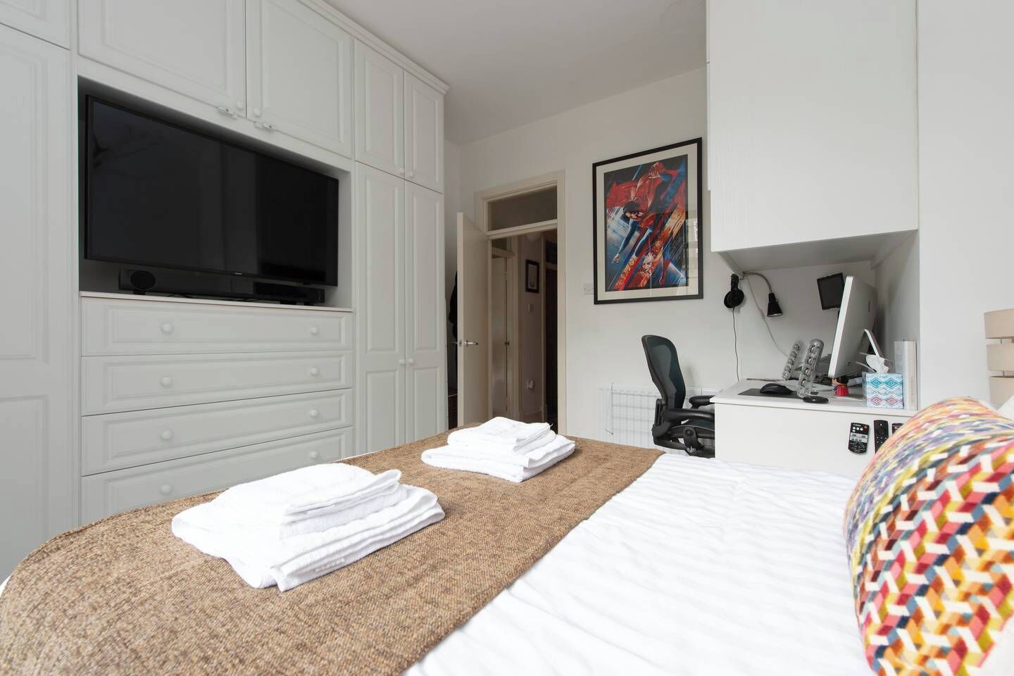 A hotel room with a bed, a desk with a computer, a TV, and a painting on the wall.