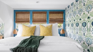Un dormitorio con cama, almohadas, una colcha y una ventana con persianas.