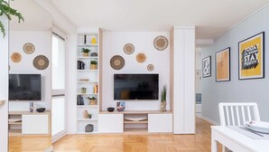 A modern living room with a large flat-screen TV, white furniture, and decorative wall art.