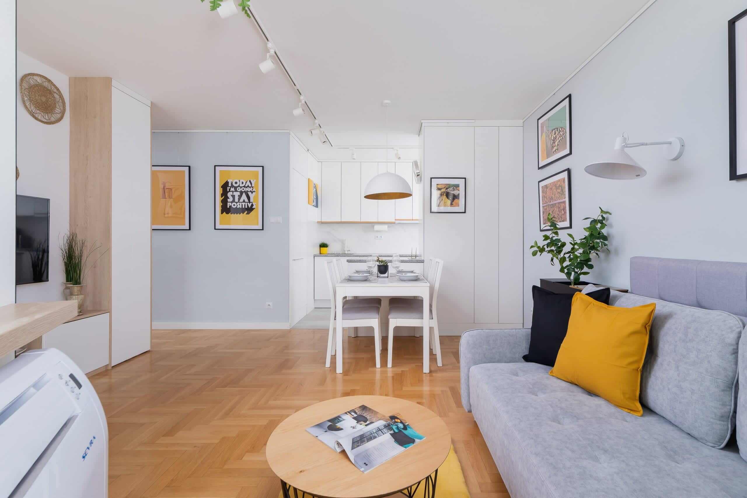 Een moderne woonkamer met een grijze bank, een salontafel en een eethoek met een witte tafel en stoelen.