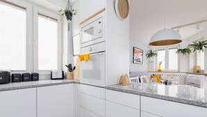 A modern kitchen with white cabinets, a granite countertop, a built-in oven, and a hanging light fixture.
