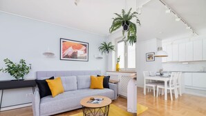 A modern living room with a grey sofa, a round coffee table, and a dining area with white chairs and a table.