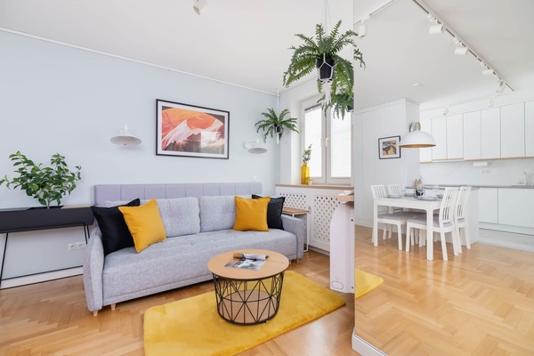 A stylish living room with a gray sofa, yellow accents, a round coffee table, and lush greenery.