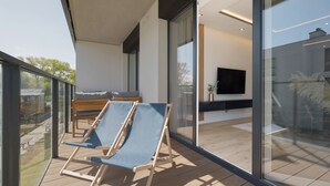 A modern balcony with two lounge chairs, a wooden bench, and a flat-screen TV in the background.