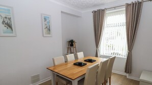A dining area with a wooden table and six chairs, a potted plant on a side table, and two framed pictures on the wall. - Brynawel (Burry Port)
