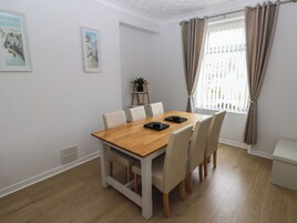 A dining area with a wooden table and six chairs, a potted plant on a side table, and two framed pictures on the wall.