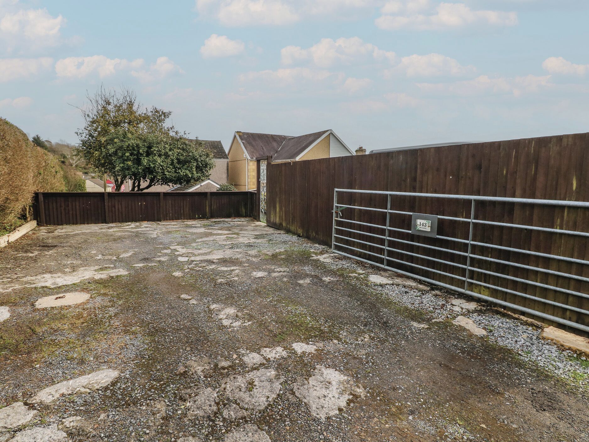 A fenced outdoor area with a gravel surface, a metal gate, and a tree.
