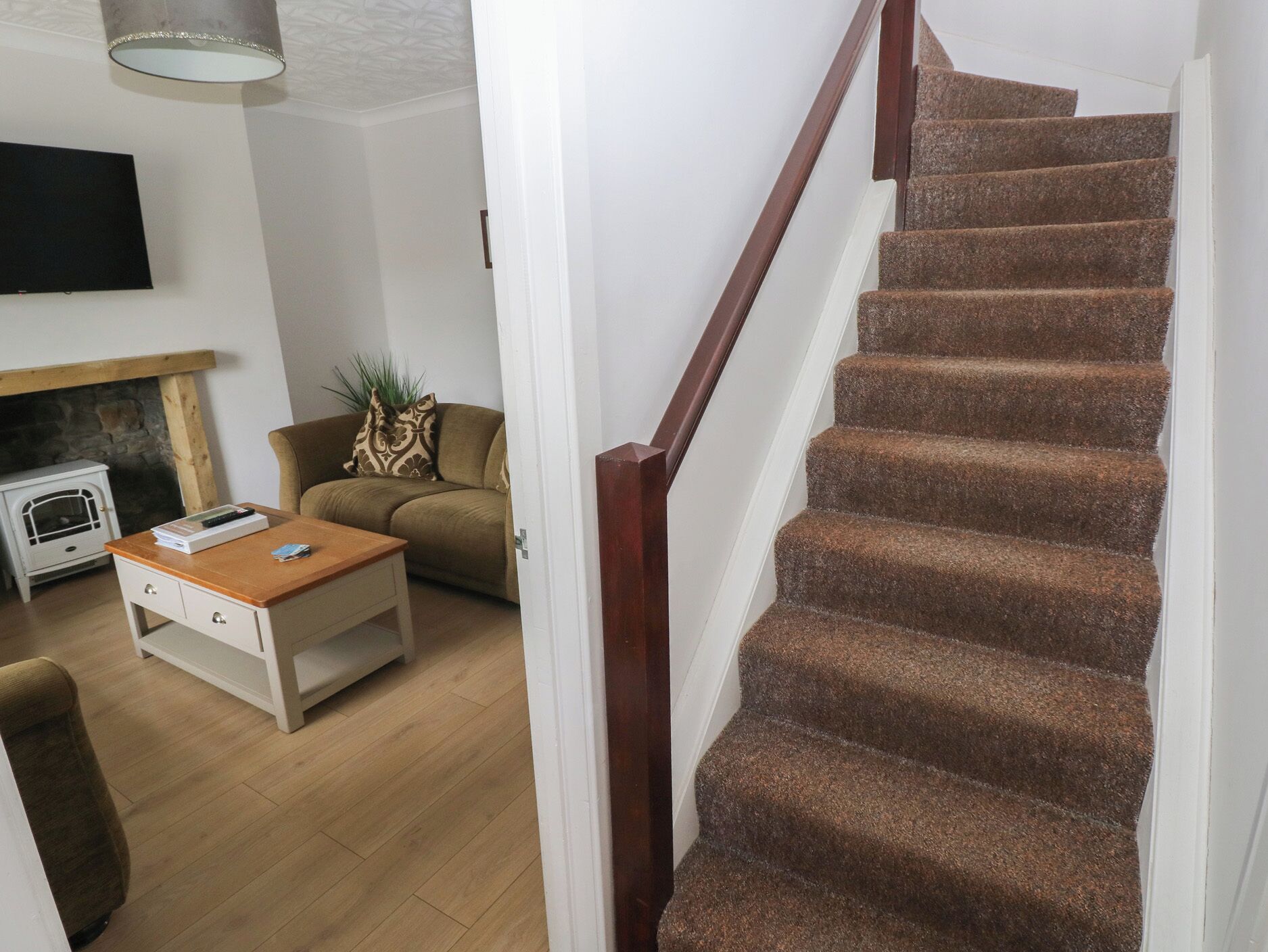 A staircase with carpeted steps and a wooden handrail, leading to a living room with a sofa, a coffee table, and a fireplace.