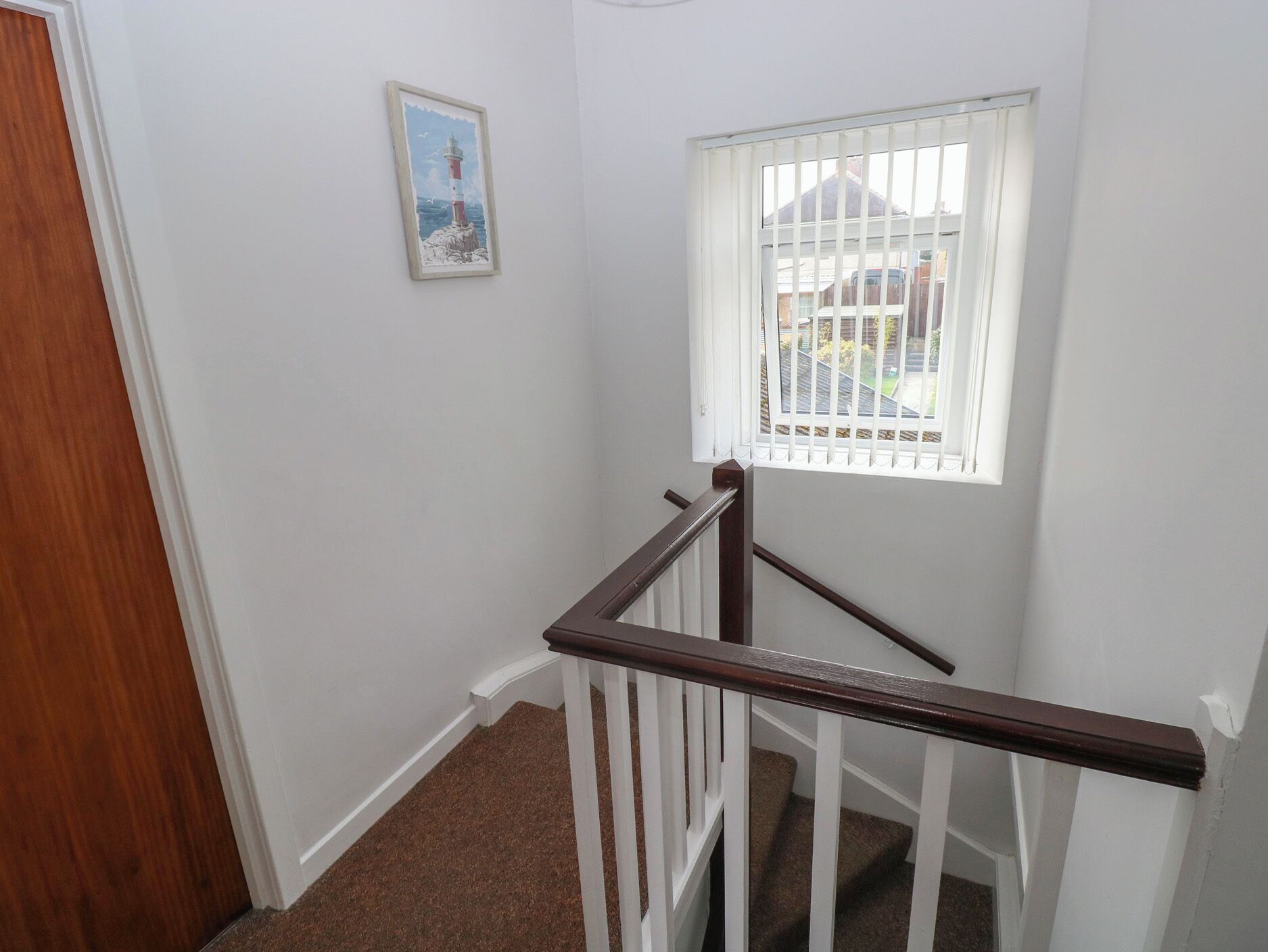 A staircase with a wooden handrail, a white wall, and a window with white blinds.