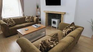 A living room with a sofa set, a coffee table, a fireplace, and a television. - Brynawel (Burry Port)