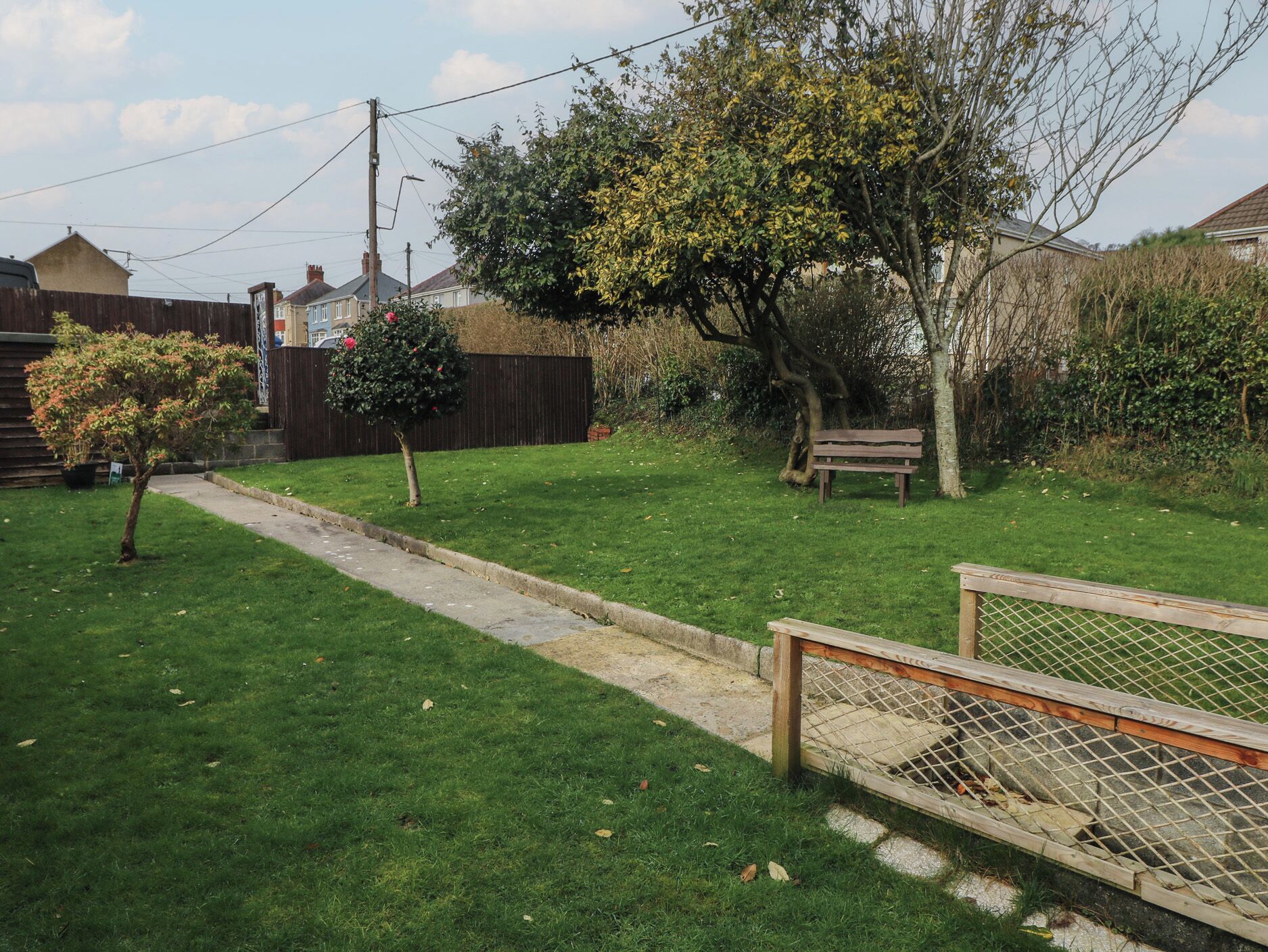 Un jardin à l’arrière d’une maison, avec un chemin pavé, une clôture en bois et un banc.
