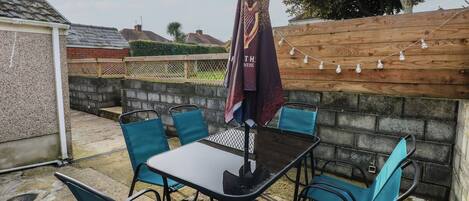 An outdoor patio with a table and chairs, a decorative umbrella, and a wooden fence.