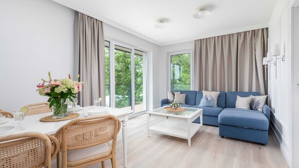 A modern living room with a blue sofa, a dining table with chairs, and a coffee table. - Apartment with 2 Bedrooms | Parking, SPA, Close to the Beach (Dziwnów)