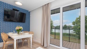 Un comedor con una mesa dispuesta para cuatro personas, un televisor de pantalla plana montado en la pared y vistas a un lago a través de amplios ventanales.