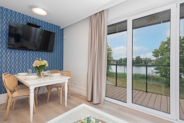 Un comedor con una mesa dispuesta para cuatro personas, un televisor de pantalla plana montado en la pared y vistas a un lago a través de amplios ventanales.