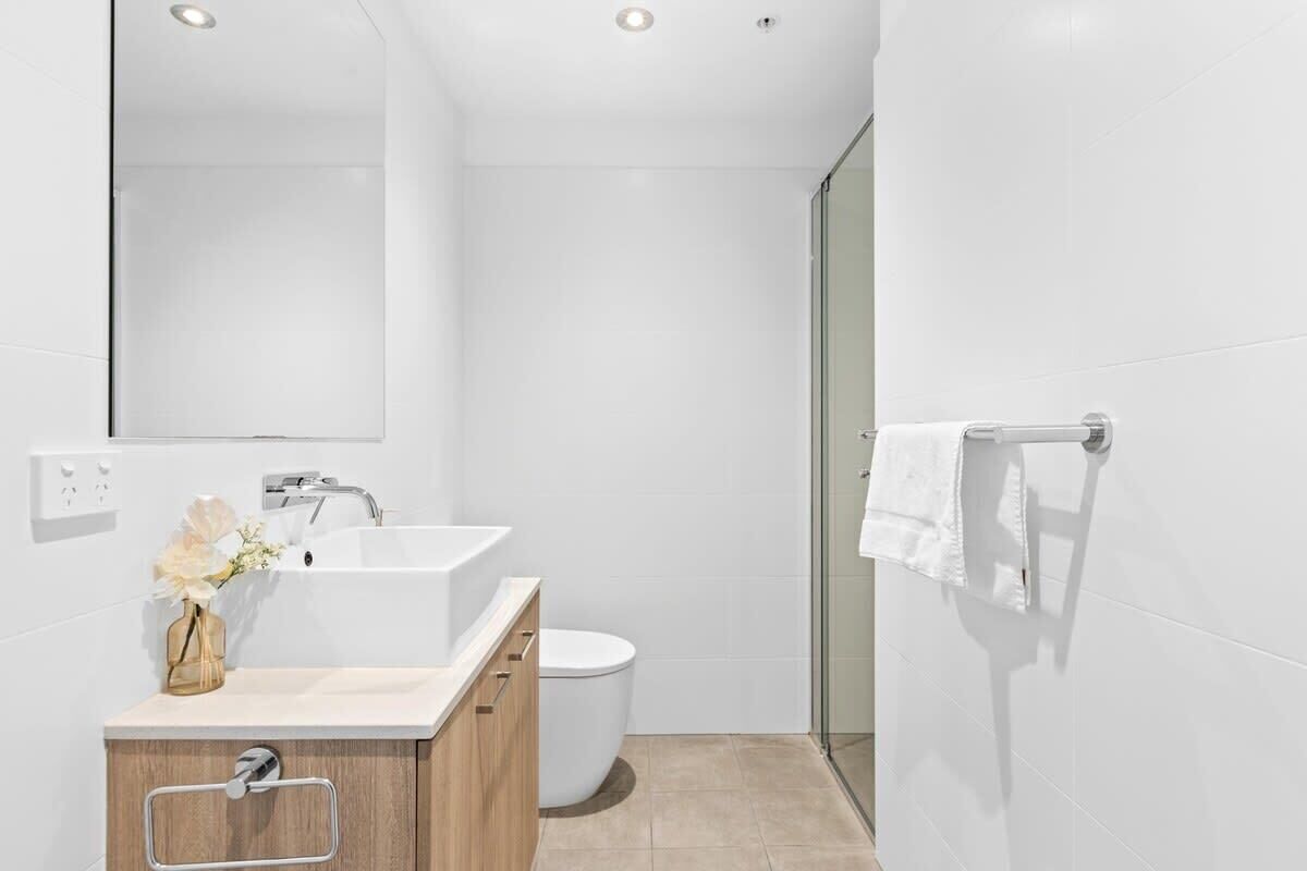 A modern bathroom with a white sink, toilet, and glass shower enclosure.