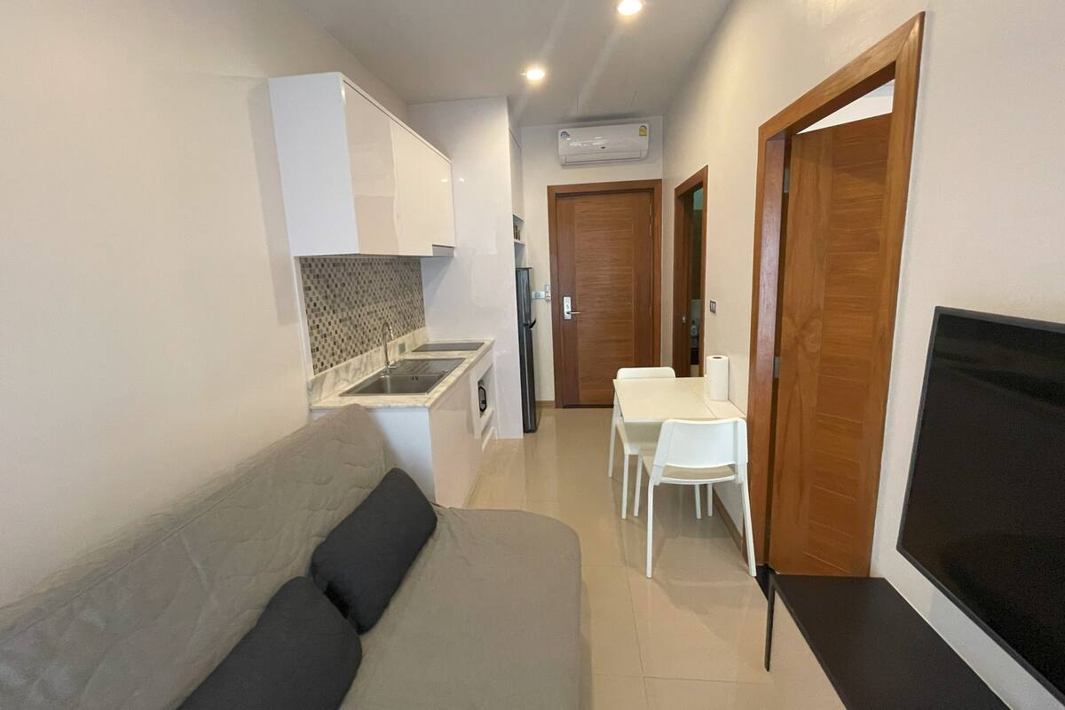 A compact living space with a kitchenette, a sofa, a dining table with chairs, and a TV.