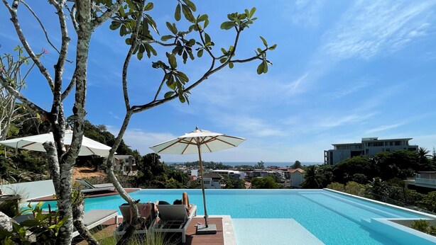 A swimming pool with lounge chairs and umbrellas, surrounded by trees and overlooking a residential area. - Apartment at Palmetto Condo by Lofty (Karon)