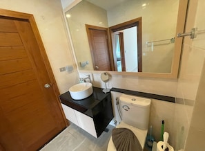 A bathroom with a wooden door, a white sink, a mirror, a toilet, and a towel hanging on the wall.