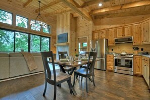 L’intérieur d’un chalet en bois comprend une table à manger, des chaises, un canapé, une cuisine équipée et de grandes fenêtres.