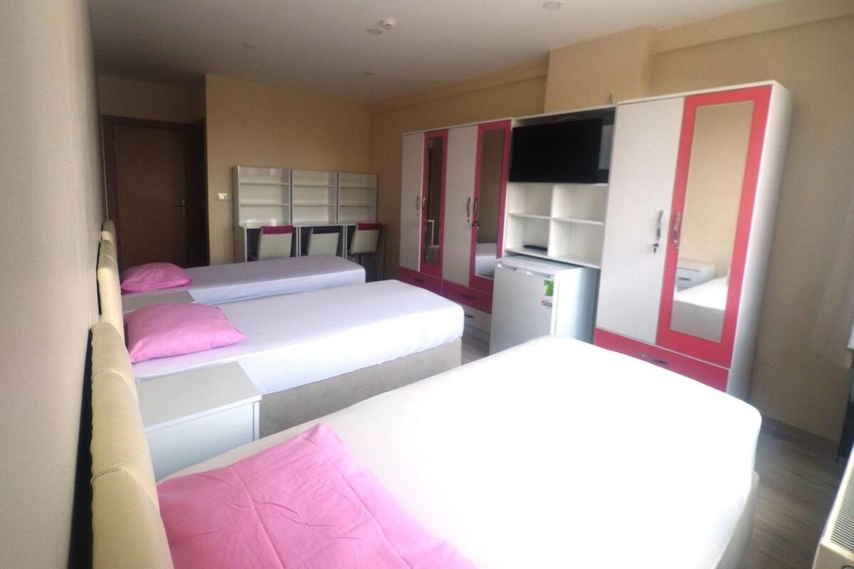 A hotel room with two beds, a desk, a wardrobe, and a television.