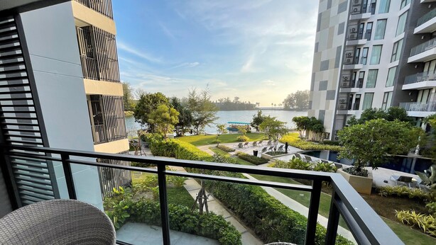 Ein Balkon mit Korbstühlen und einem Tisch, der auf eine angelegte Grünfläche mit Pool und modernen Gebäuden blickt.