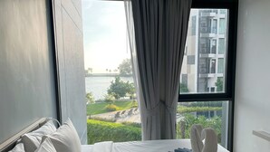 Ein Hotelzimmer mit einem großen Bett, Blick auf ein Gewässer und einem modernen Gebäude im Hintergrund.