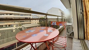 Un balcon avec une table et des chaises rouges, une vue sur des immeubles et une enseigne indiquant « HÔTEL ».