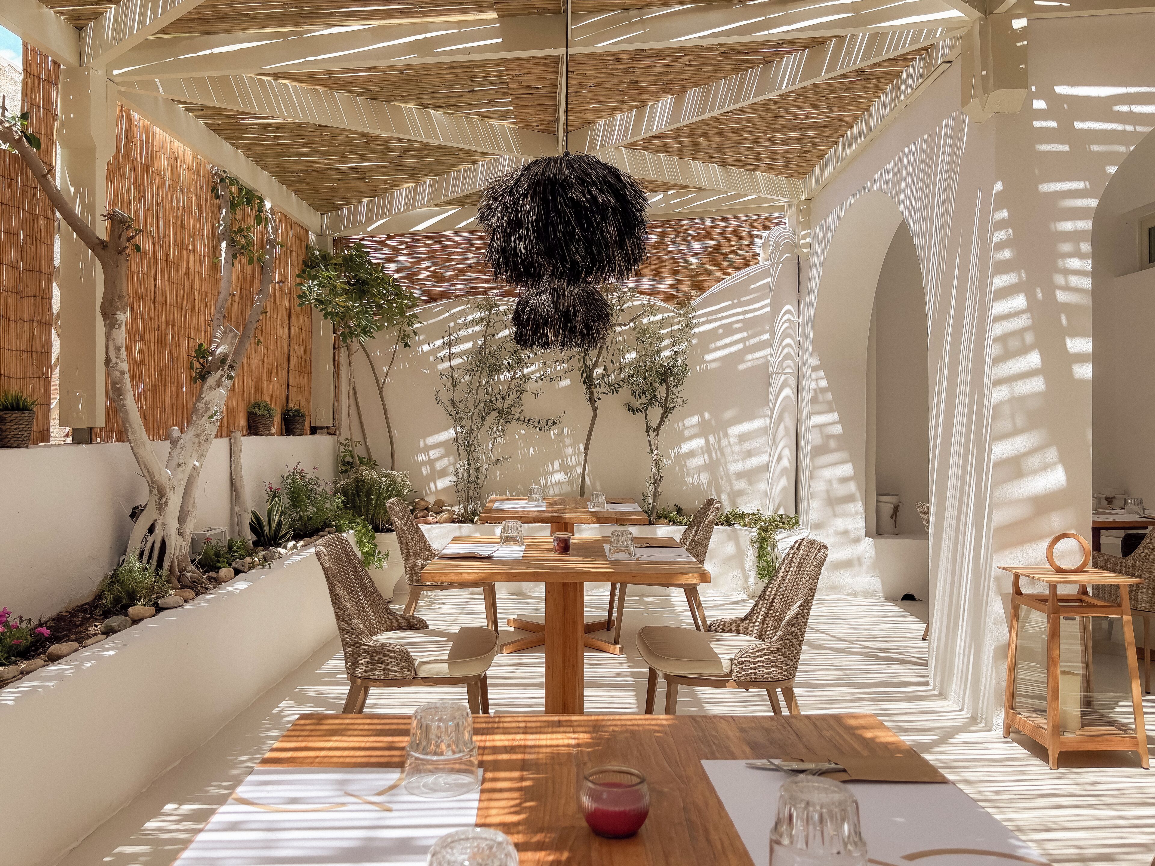 An indoor dining area with a wooden table, wicker chairs, and a hanging light fixture.