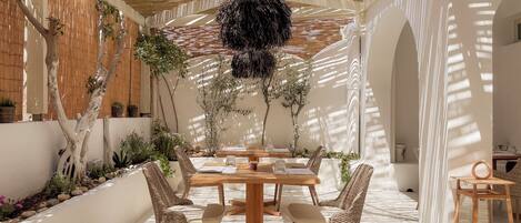 An indoor dining area with a wooden table, wicker chairs, and a hanging light fixture.