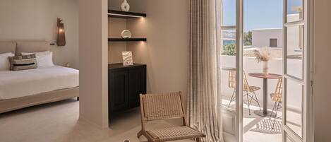 Un dormitorio moderno con una cama, una silla de madera, una mesita con jarrones y vistas al exterior a través de un ventanal.