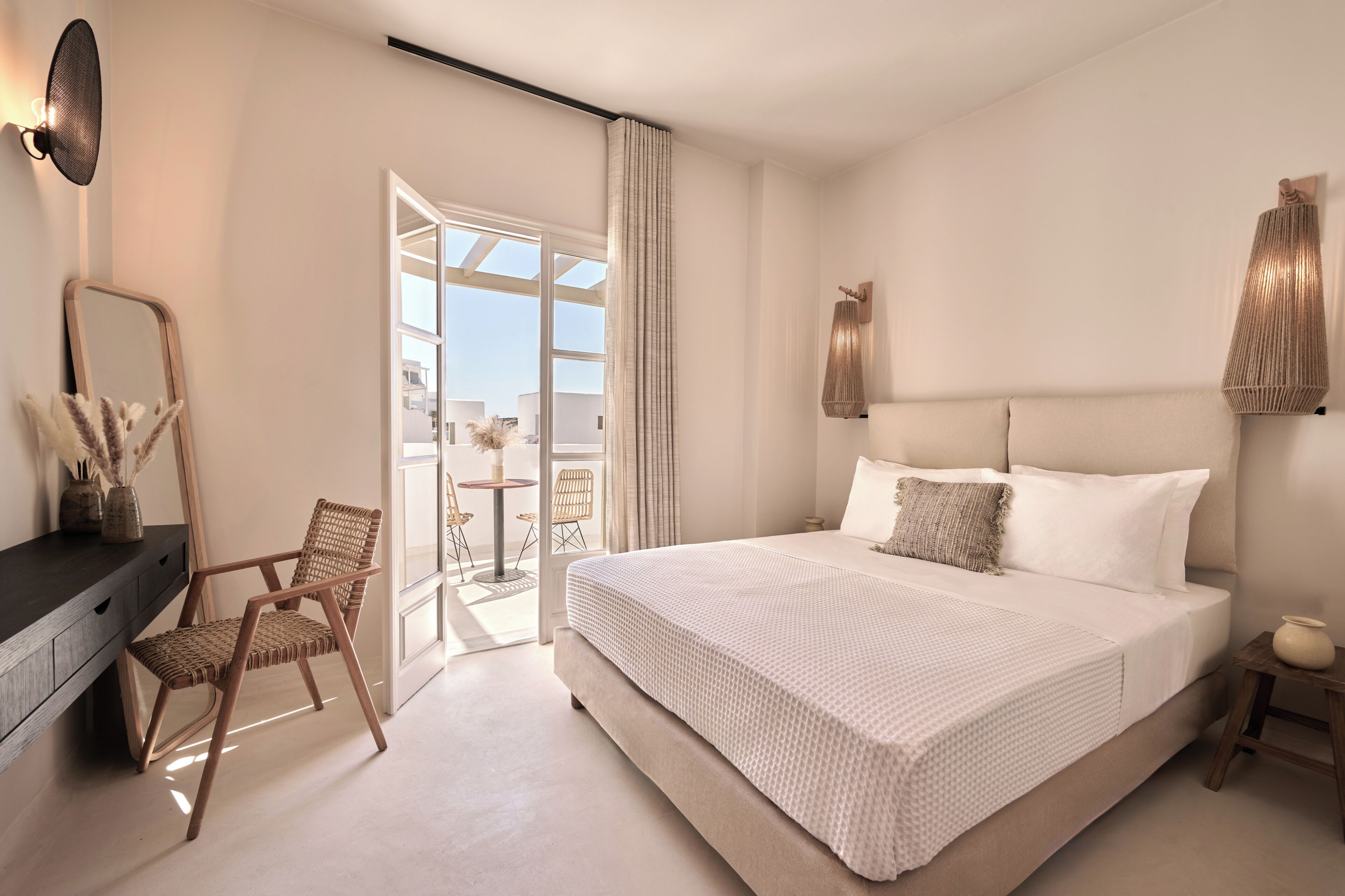 A bedroom with a large bed, a chair, a desk, and a view of the outdoors.