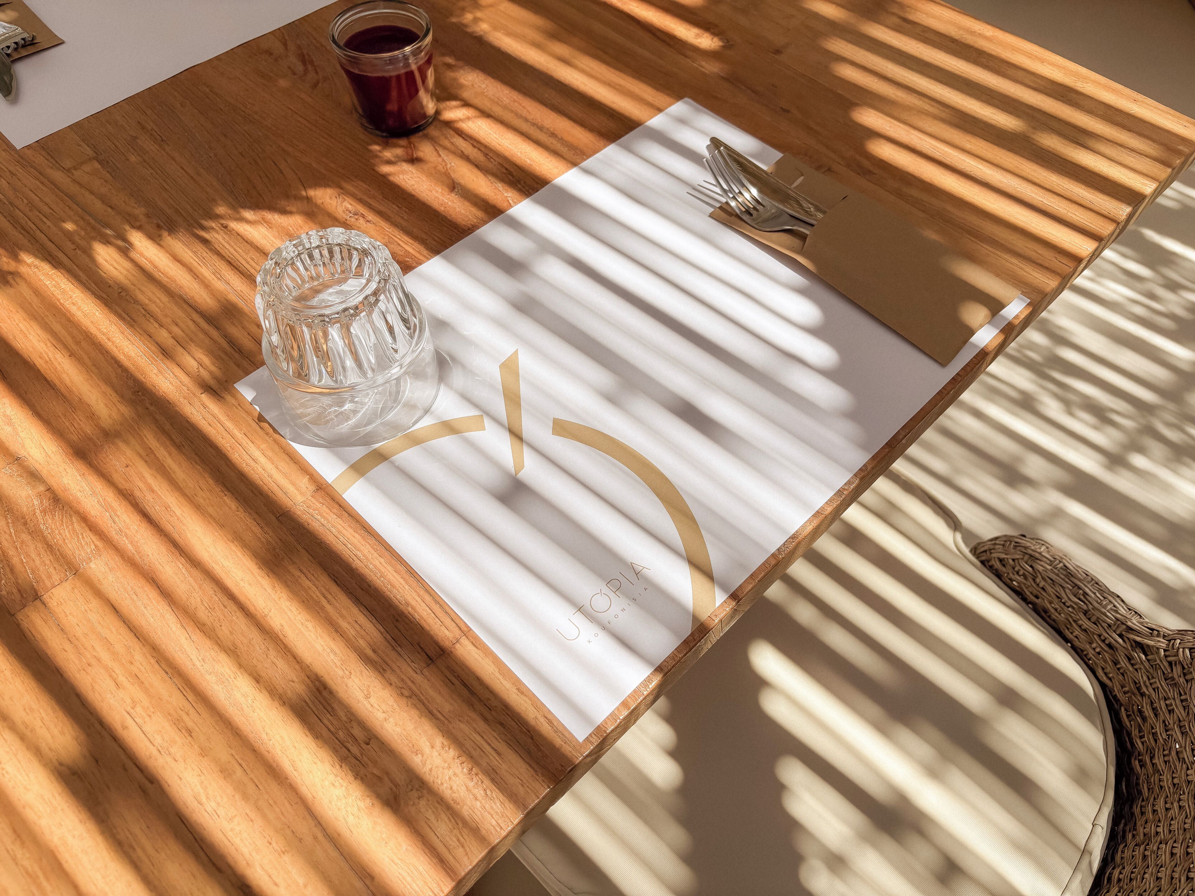 Een houten tafel met een witte placemat, een glas en een vork.