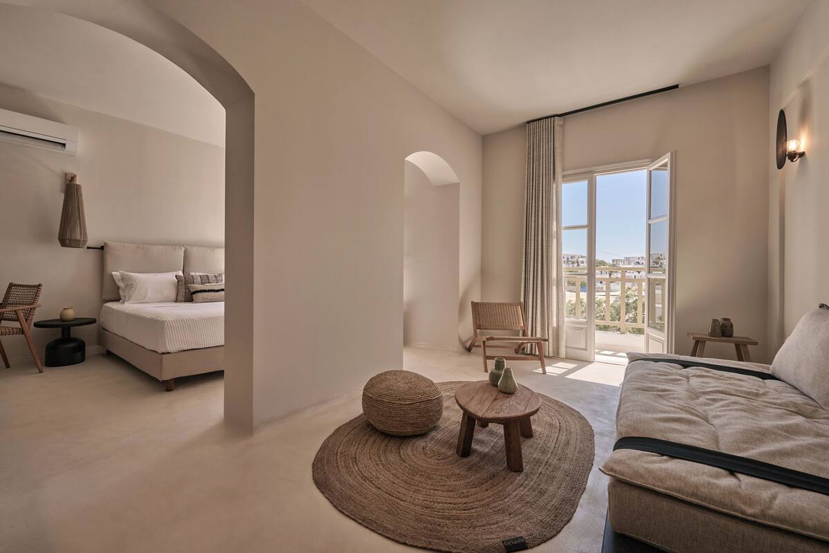 Une chambre d’hôtel moderne, dotée d’un lit, d’un canapé, d’un tapis rond et offrant une vue sur la ville grâce à de grandes fenêtres.