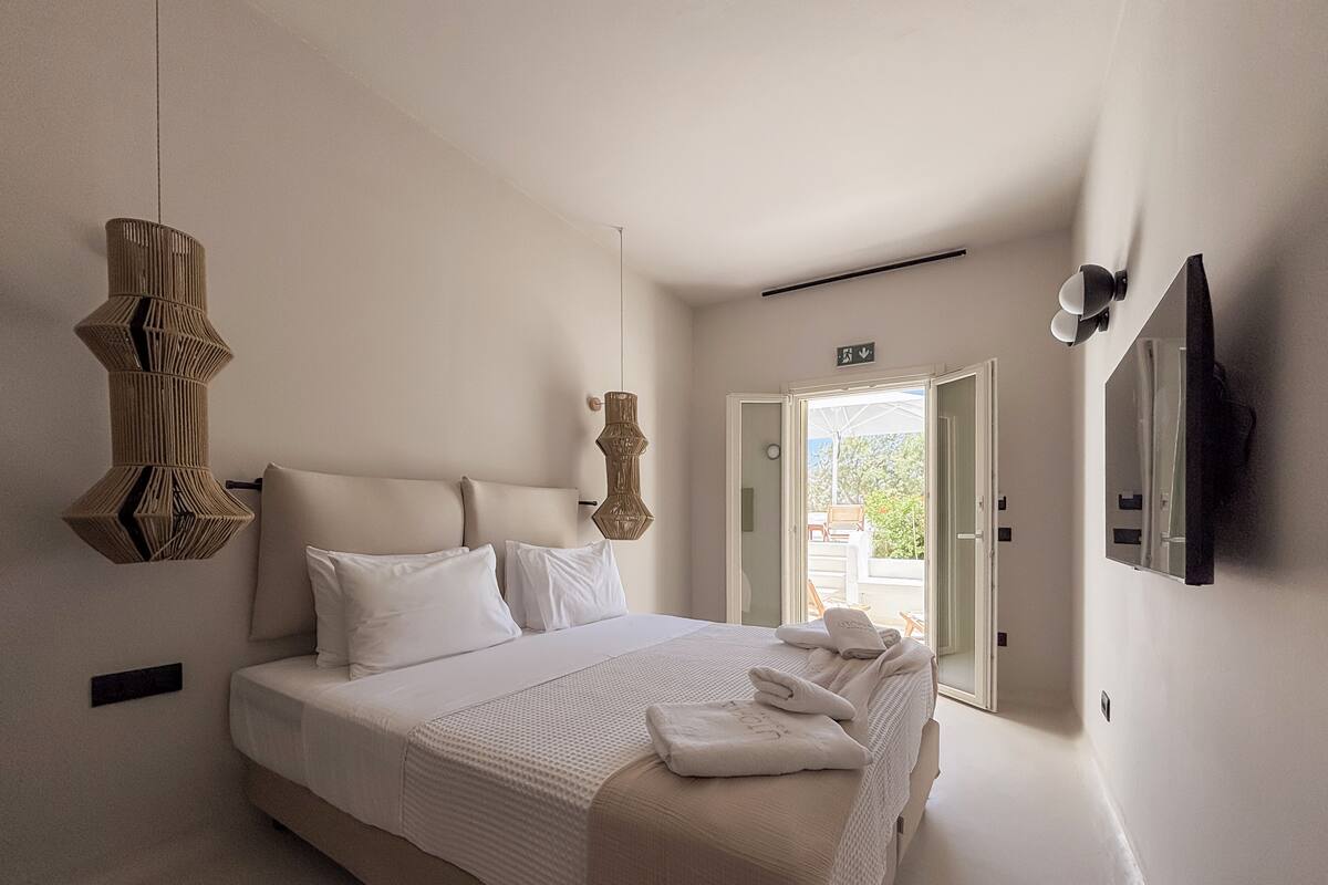Une chambre d’hôtel comprenant un lit, un luminaire suspendu, une porte donnant sur un espace extérieur et un téléviseur fixé au mur.