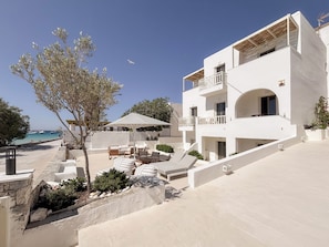 A white building with balconies, outdoor seating, and a view of the sea. - Utopia Hotel (Koufonisia)