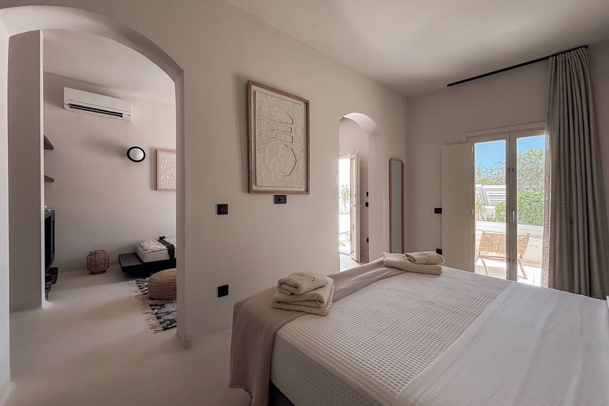 Une chambre dotée d’un grand lit, d’un coin salon avec un canapé, d’une table à manger et offrant une vue sur l’extérieur.
