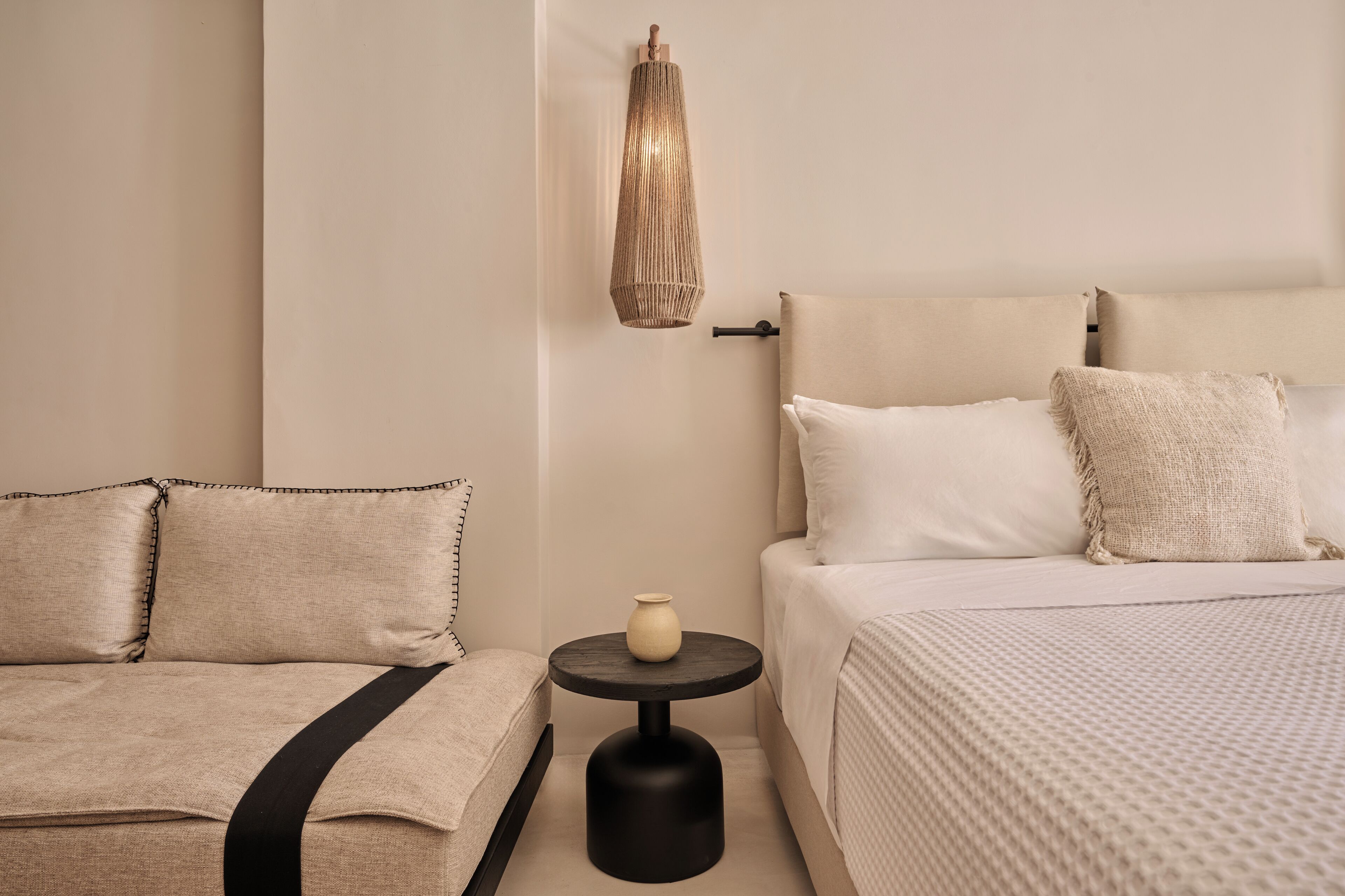 A hotel room with two beds, a round black table, a vase, and a wall-mounted light fixture.