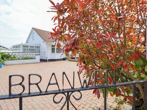 Stroll up the paved driveway to the charming BRANWEN residence, surrounded by a lush garden and a low wall.