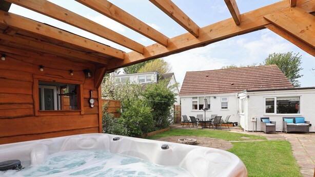 Een hottub in een houten chalet met uitzicht op een wit huis en een tuin.
