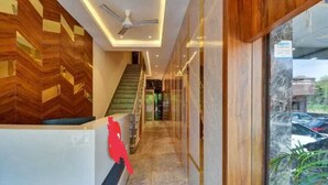 Zona de recepción de un hotel con un muro de madera, una escalera y vistas a coches aparcados afuera.